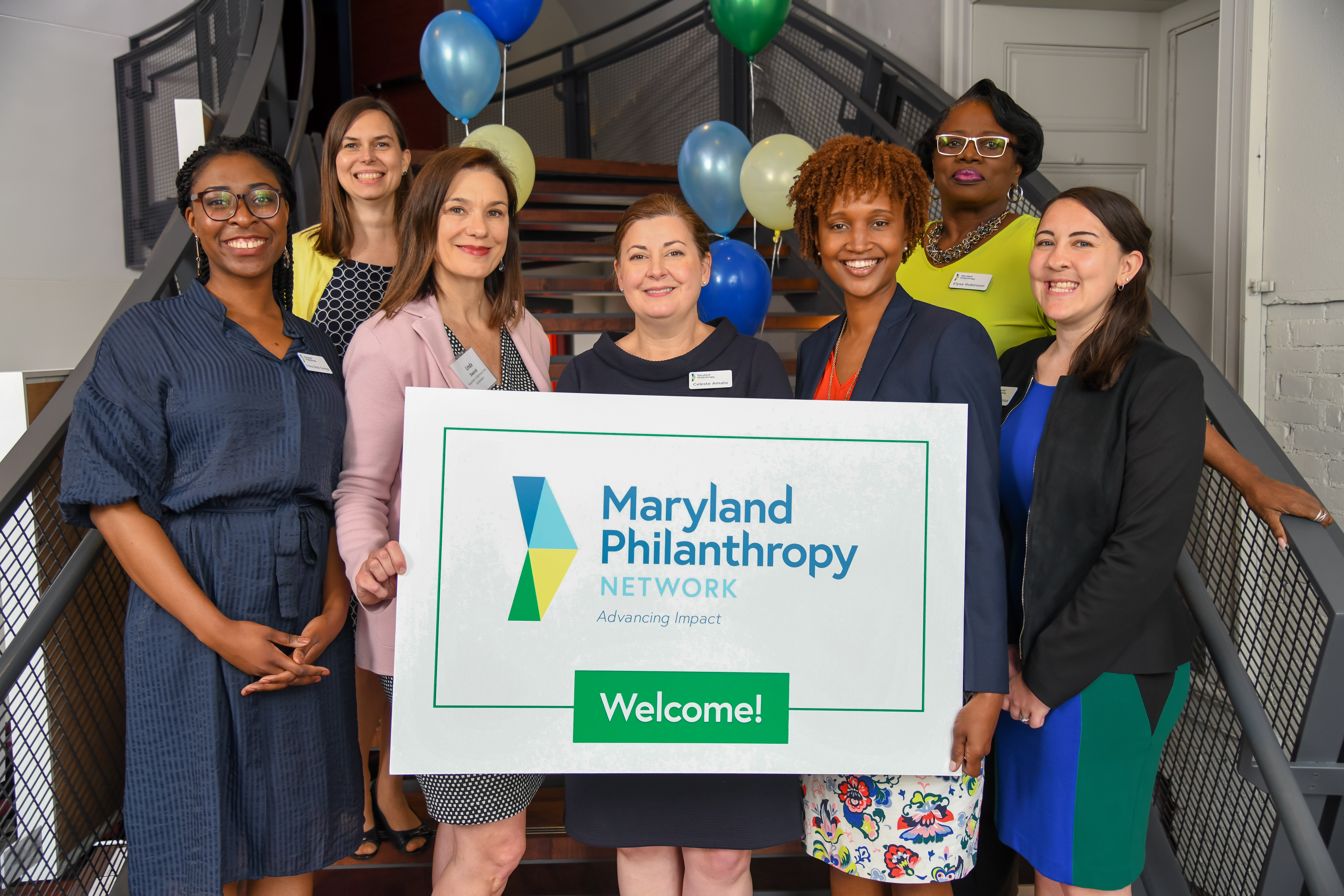 Seven women on stairs holding a Welcome to Maryland Philanthropy Network sign.