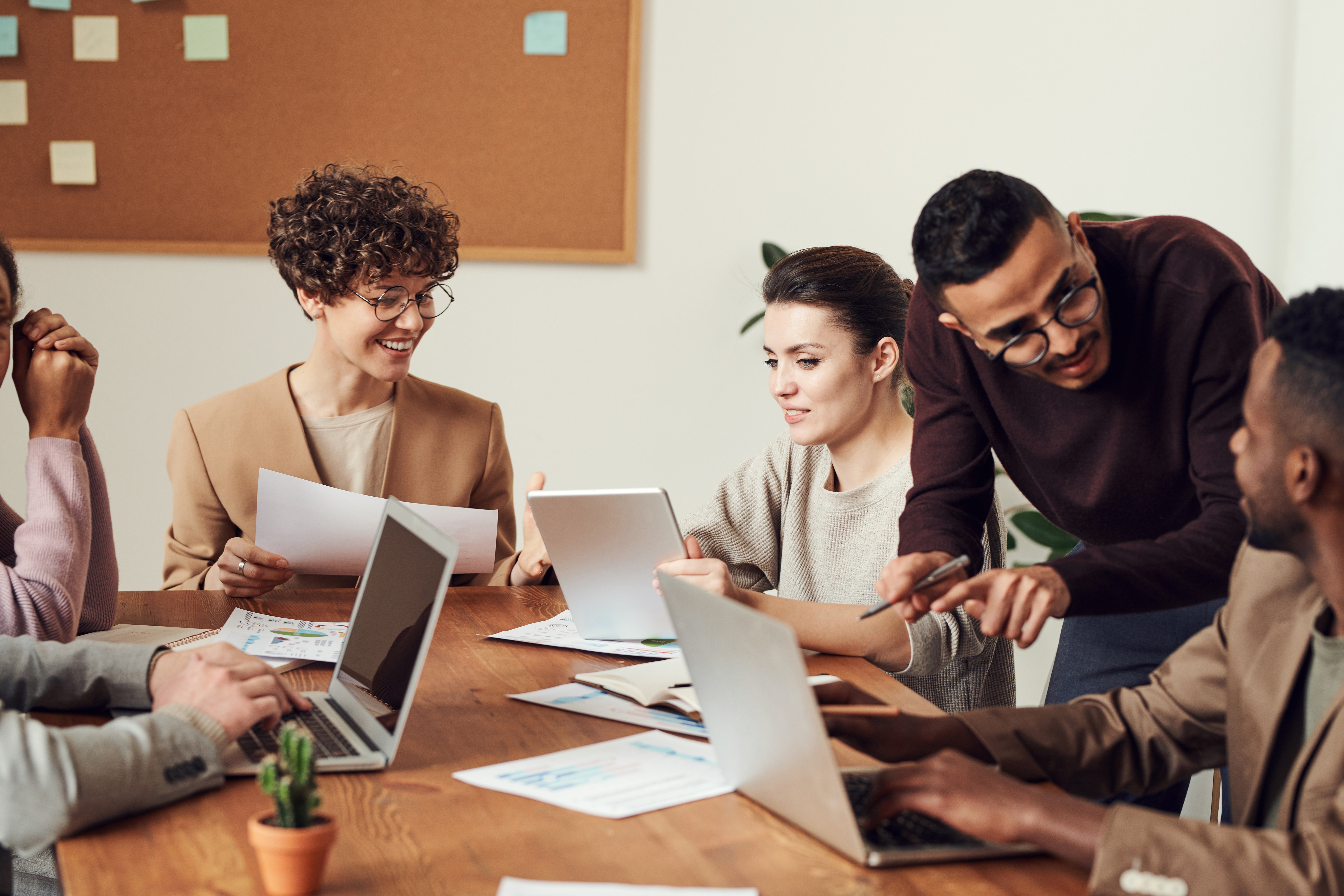 Group of people in business meeting viewing documents and laptops at a table bulletin board with s