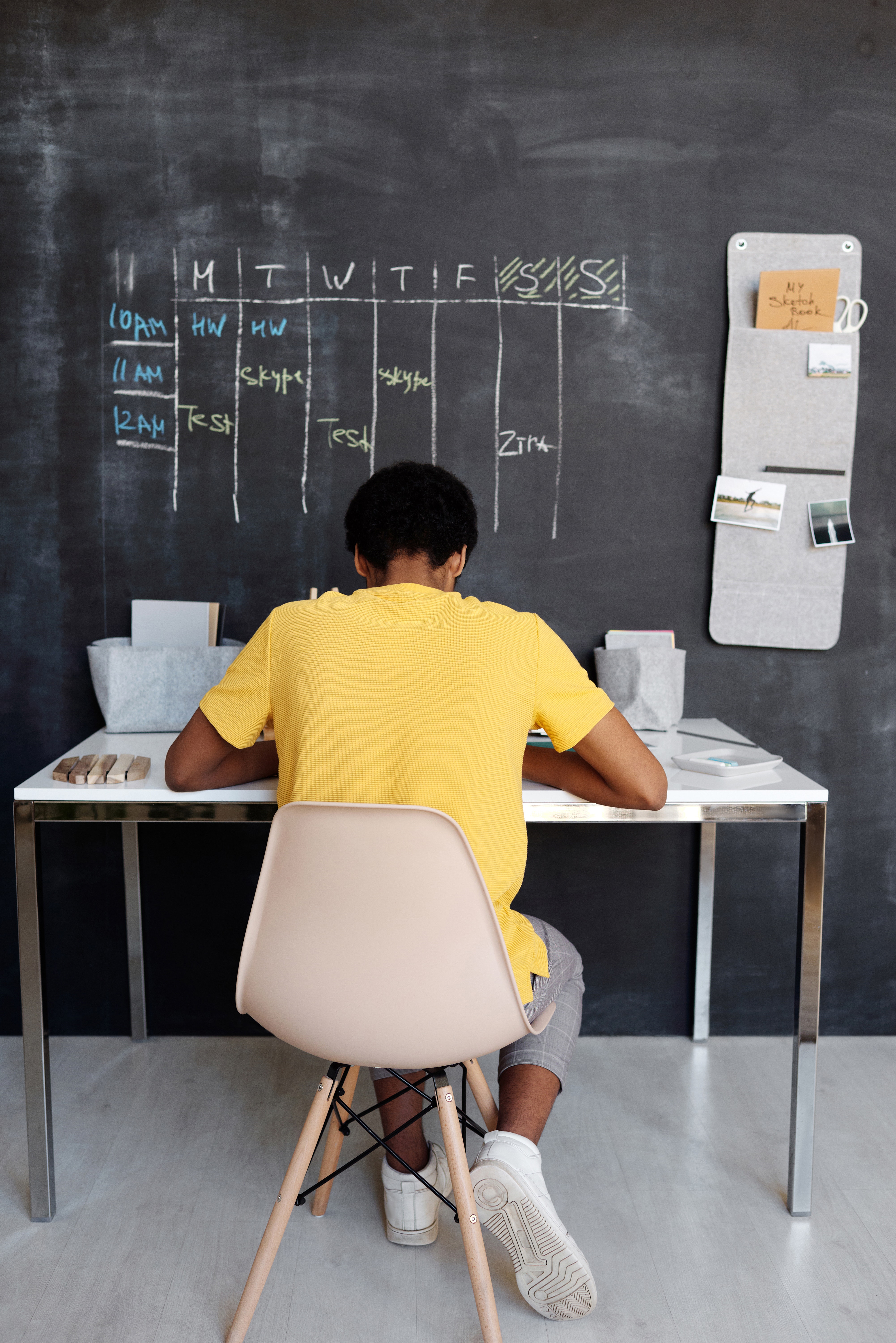 Boy in yellow shirt at desk facing a chalk board with a schedule