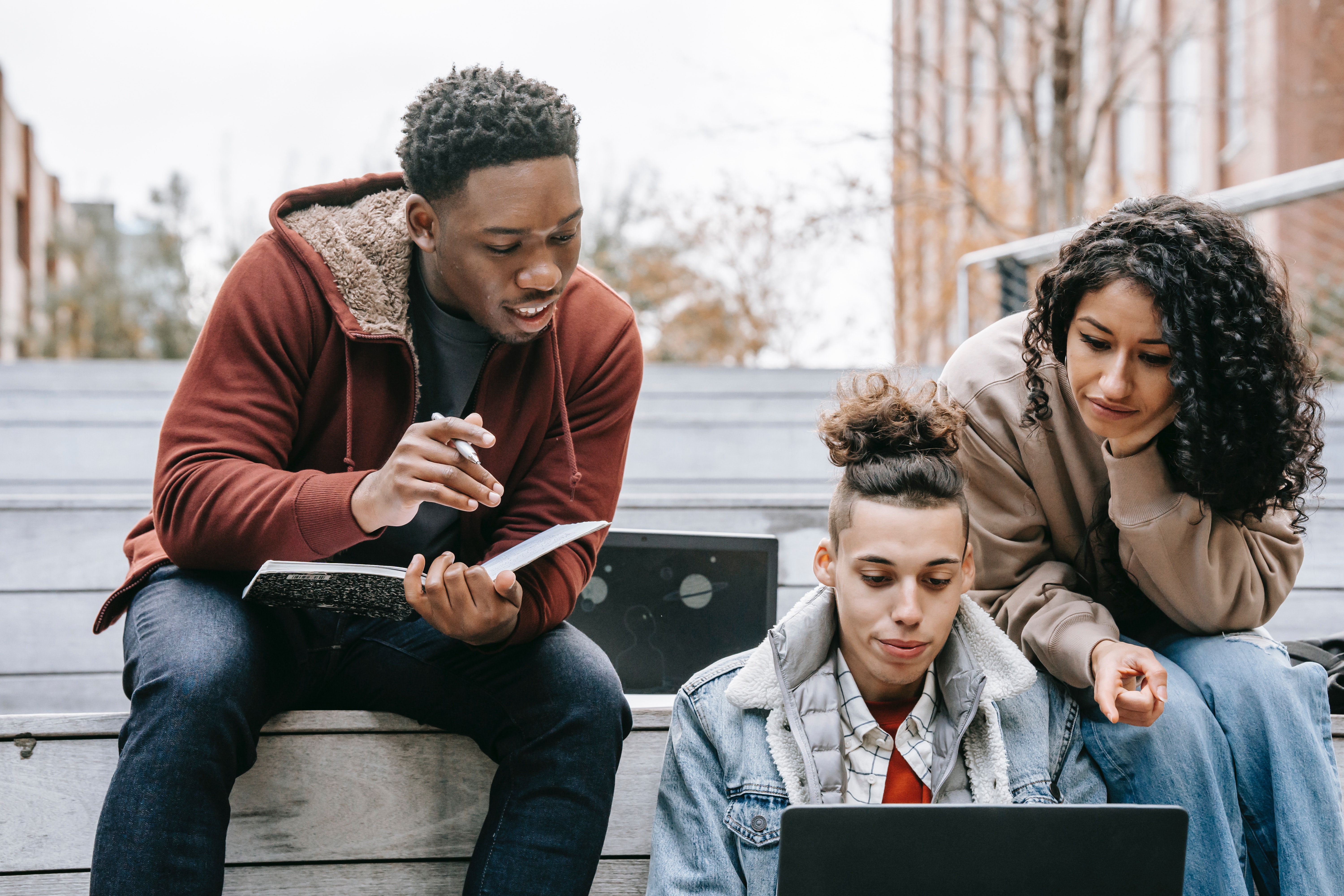 Youth outside on stone steps. All are viewing content on a laptop.